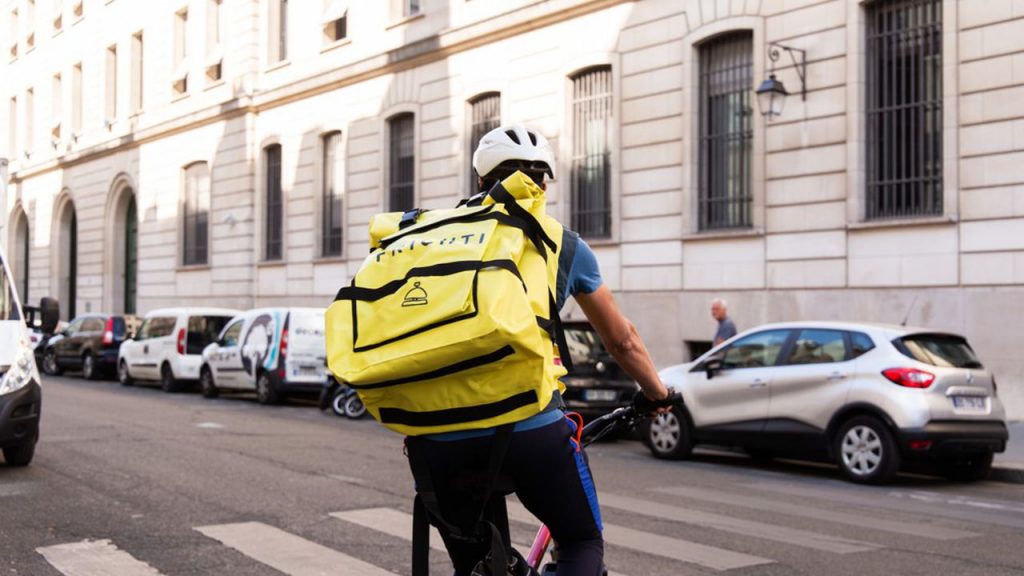 Il s'agit d'un homme à vélo qui effectue une livraison à domicile de nourriture. Il porte un sac à dos avec un logo.